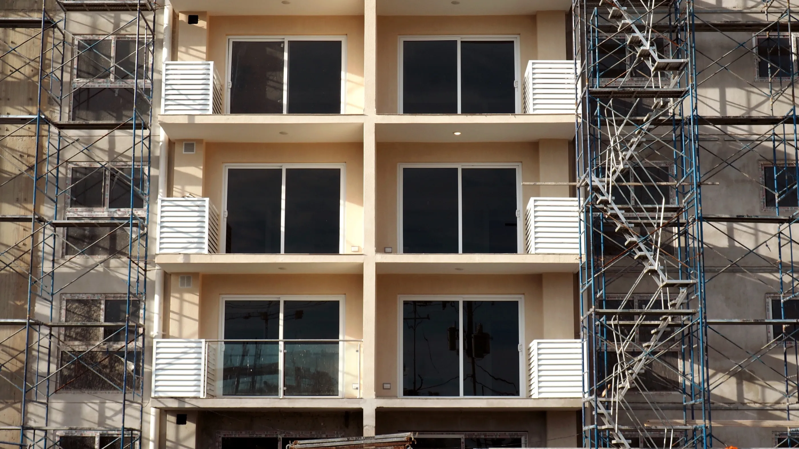Evening light on the balconied facade of a mid-rise under construction in Costa Rica, scaffolding climbing both sides
