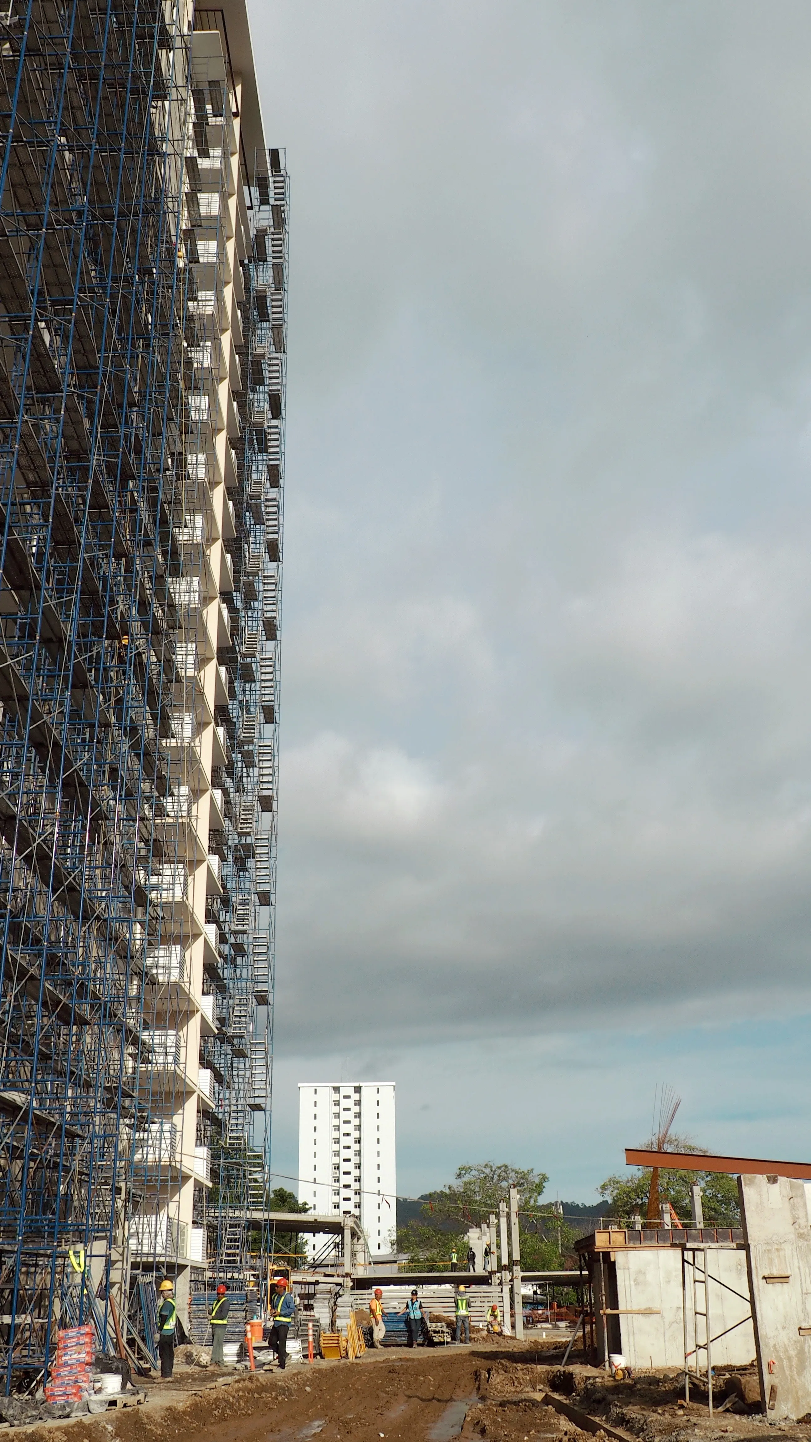 A high-rise under construction in Costa Rica, scaffolding wrapping the concrete frame under a cloudy sky